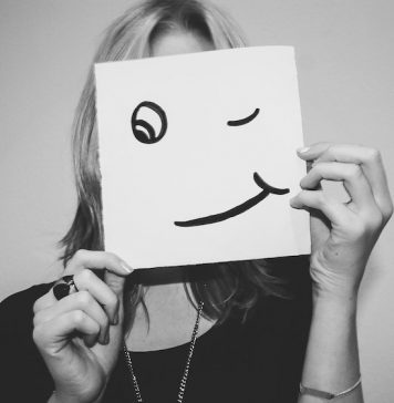 Woman holding up a smiling face over her own face