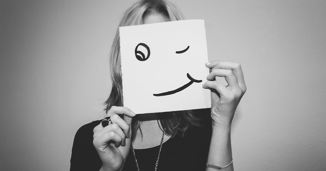 Woman holding up a smiling face over her own face