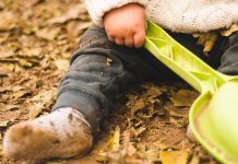 Baby with muddy socks sitting in autumn leaves