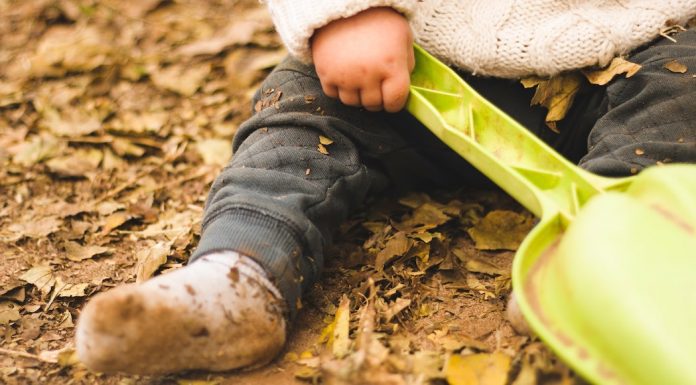 Baby with muddy socks sitting in autumn leaves
