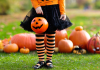 Child in front of pumpkins dressed in orange and black with a jackolantern bucket for Halloween in October