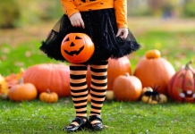 Child in front of pumpkins dressed in orange and black with a jackolantern bucket for Halloween in October