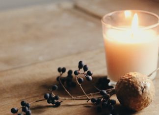 A lit candle next to nuts and dried berries on a wooden table