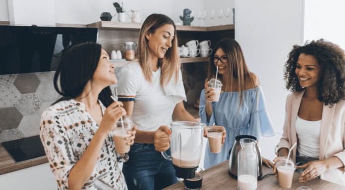 4 women friends smiling and making drinks together in a kitchen