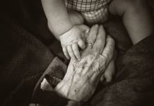 Older adult hand reaching towards a baby in black and white photo