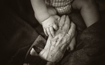 Older adult hand reaching towards a baby in black and white photo