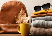 A pile of fall colored clothing with sunglass, a coffee mug, a leaf, and a brown bag