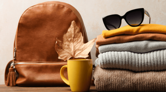 A pile of fall colored clothing with sunglass, a coffee mug, a leaf, and a brown bag