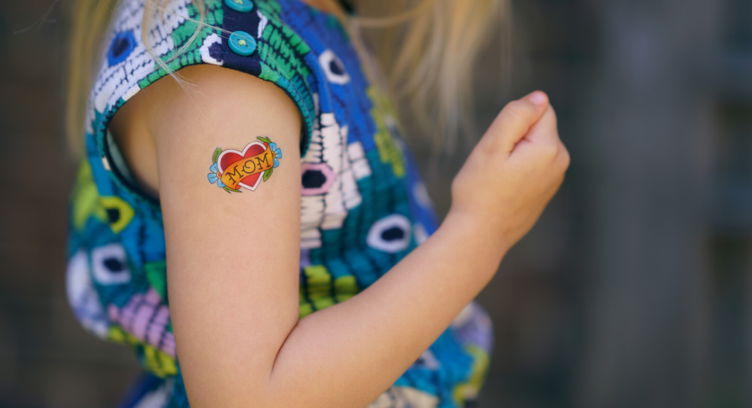 image of a young child showing off her bicep with a temporary tattoo of a heart with Mom in the middle