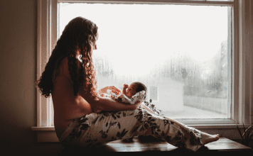 Mother with long hair and pants holding and staring down at her new baby