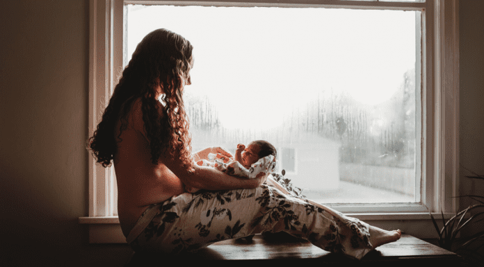 Mother with long hair and pants holding and staring down at her new baby