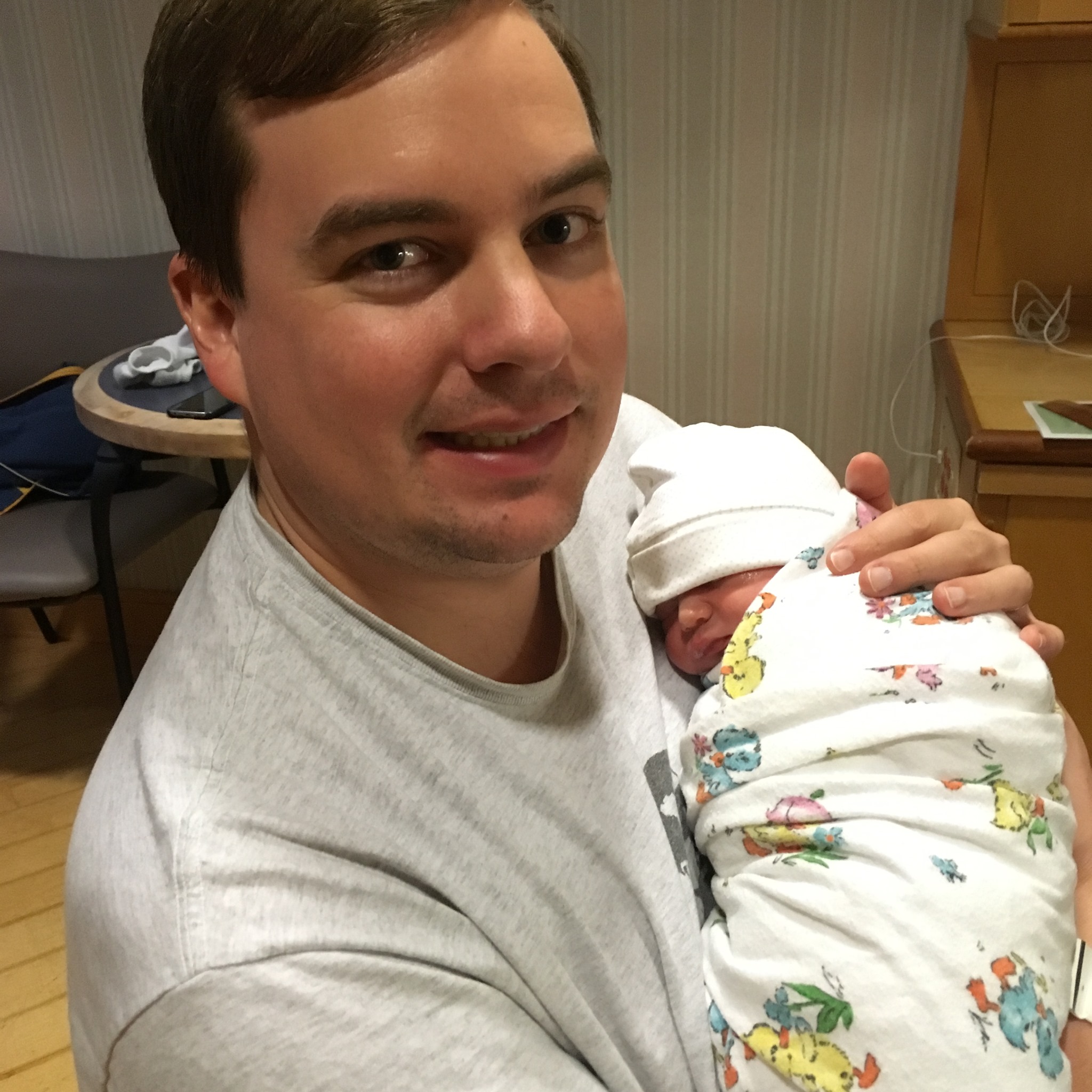 A first time father holding his newborn baby and smiling cautiously at the camera
