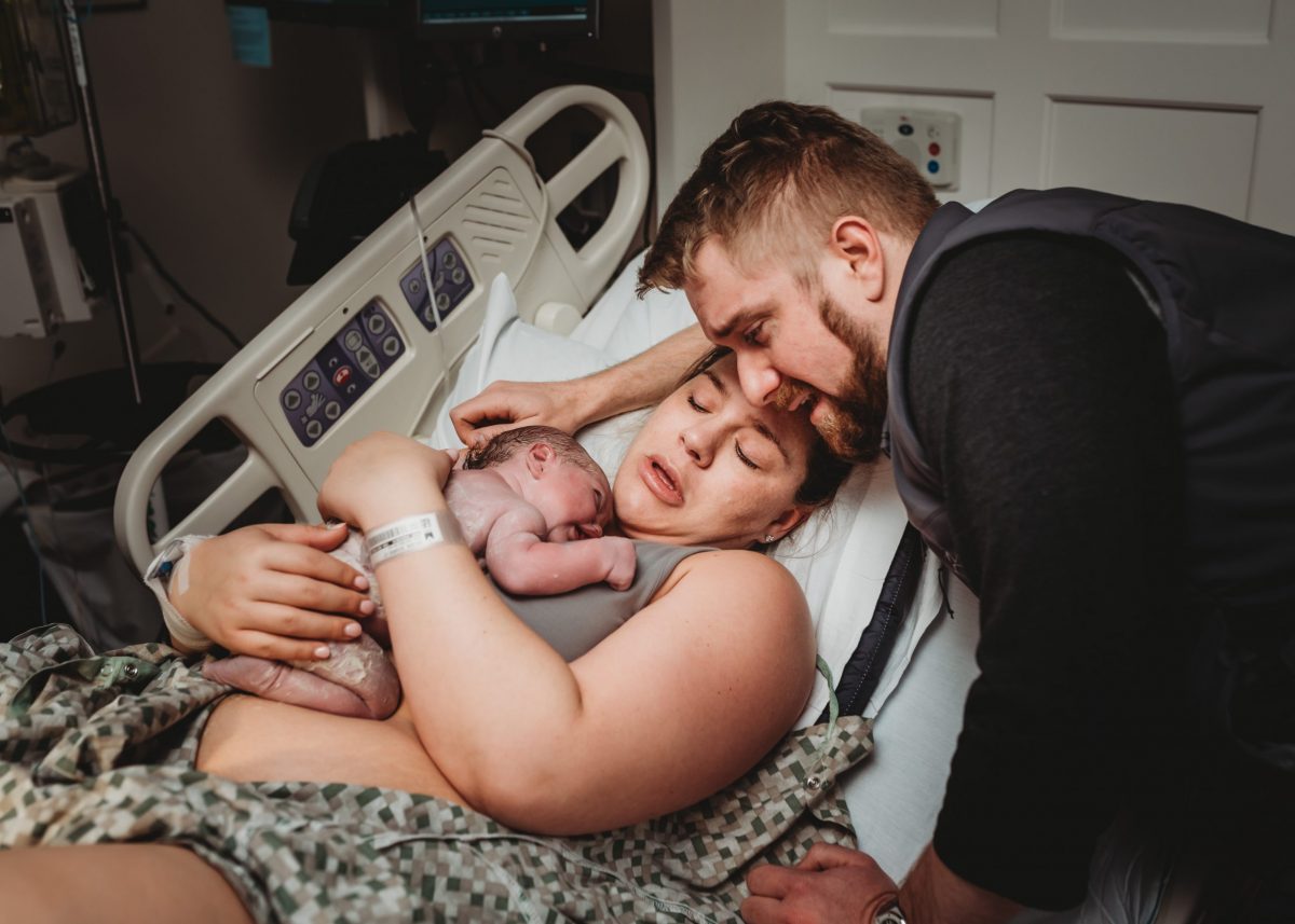 A mother holding her newborn baby on her chest as the Father looks at his baby in awe