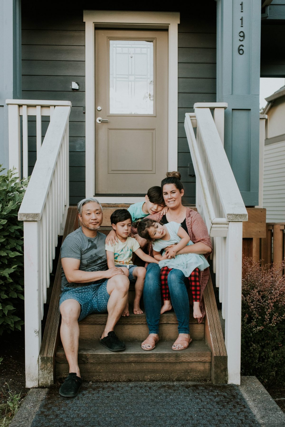 Family of father, mother, and three kids sitting on their front porch