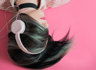 women with black and green hair covering her face laying down on a pink background with headphones on