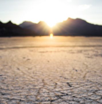 Dry desert with sun behind mountains