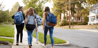 Four middle girls with backpacks walking away down a sidewalk