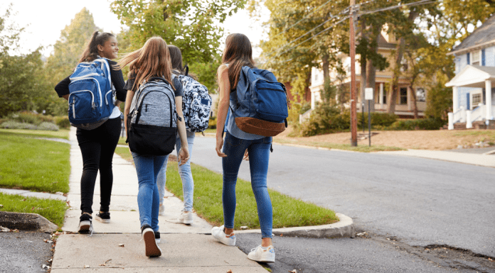 Four middle girls with backpacks walking away down a sidewalk