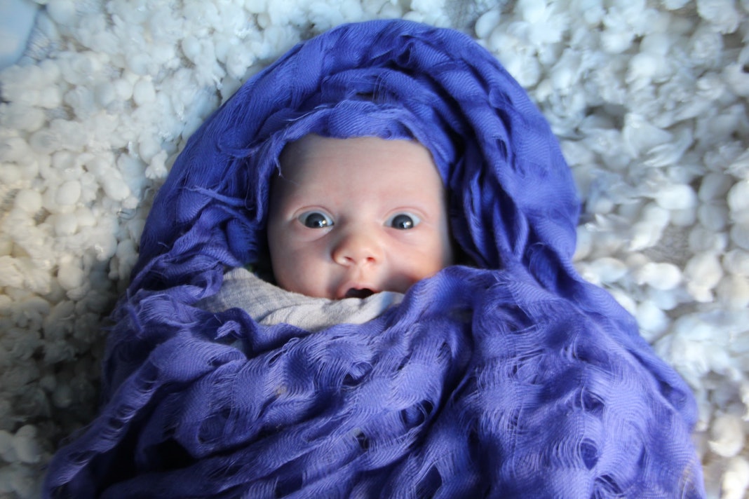 baby wrapped in indigo fabric with a look of surprise on their face