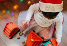 image from above of a child playing with toys on the floor wearing a christmas hat that says Santa's Helper