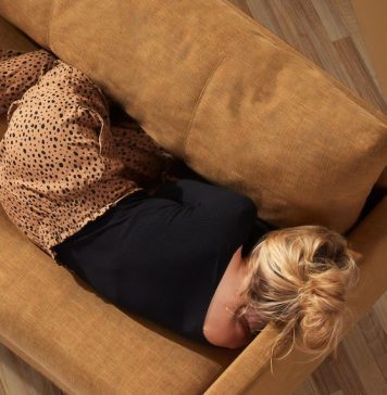 Woman lying on couch with back to camera, hiding face