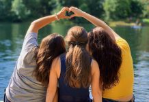 Three kids sit by river in the summertime, making a heart shape