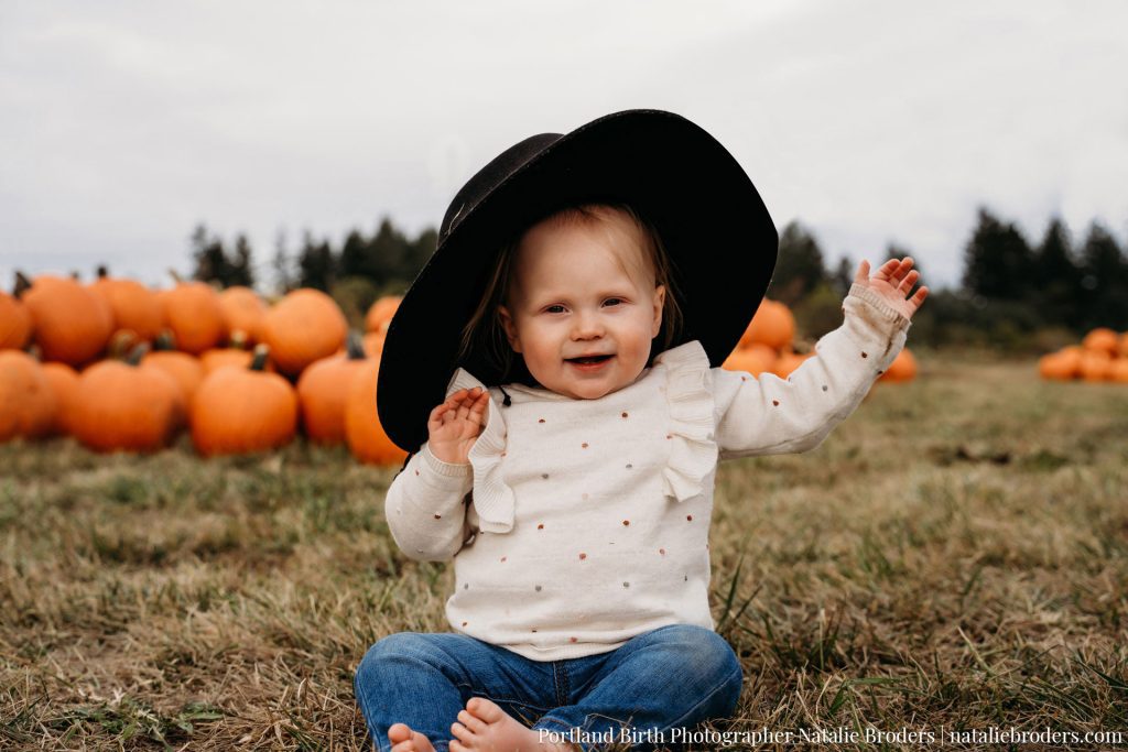 A toddler in a big hat in front of pumpkins at Plumper Pumpkin Patch in the Fall