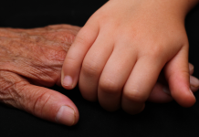 An up close image of Intergenerational holding hands, one elderly and one of a child