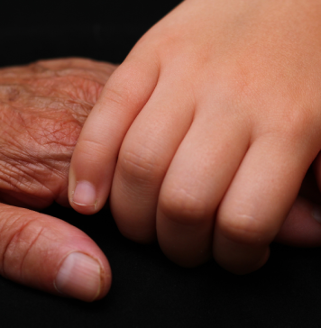 An up close image of Intergenerational holding hands, one elderly and one of a child