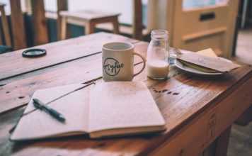 Open journal sits on a wooden cafe table with a coffee and creamer nearby