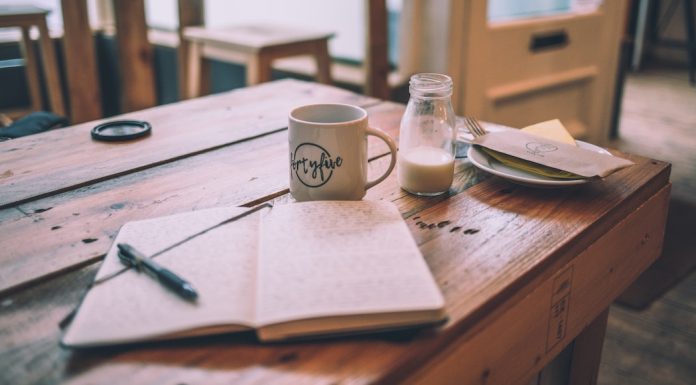 Open journal sits on a wooden cafe table with a coffee and creamer nearby