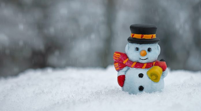 A snowman figurine sits in a pile of snow.