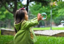 Young girl plays with bubbles in a green coat