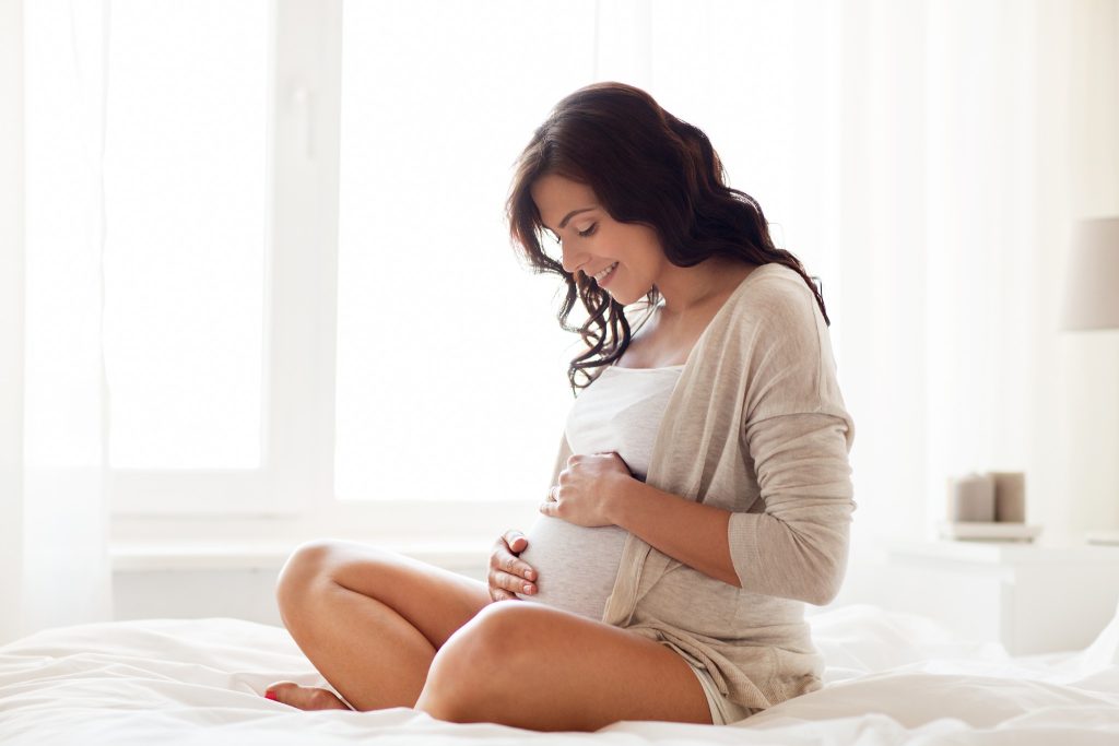 Becoming a surrogate brings all kinds of benefits. Image of pregnant woman sitting on her bed.