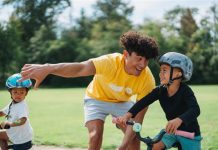 Image of young male instructor encouraging a boy learning to ride a bicycle.