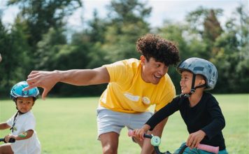 Image of young male instructor encouraging a boy learning to ride a bicycle.