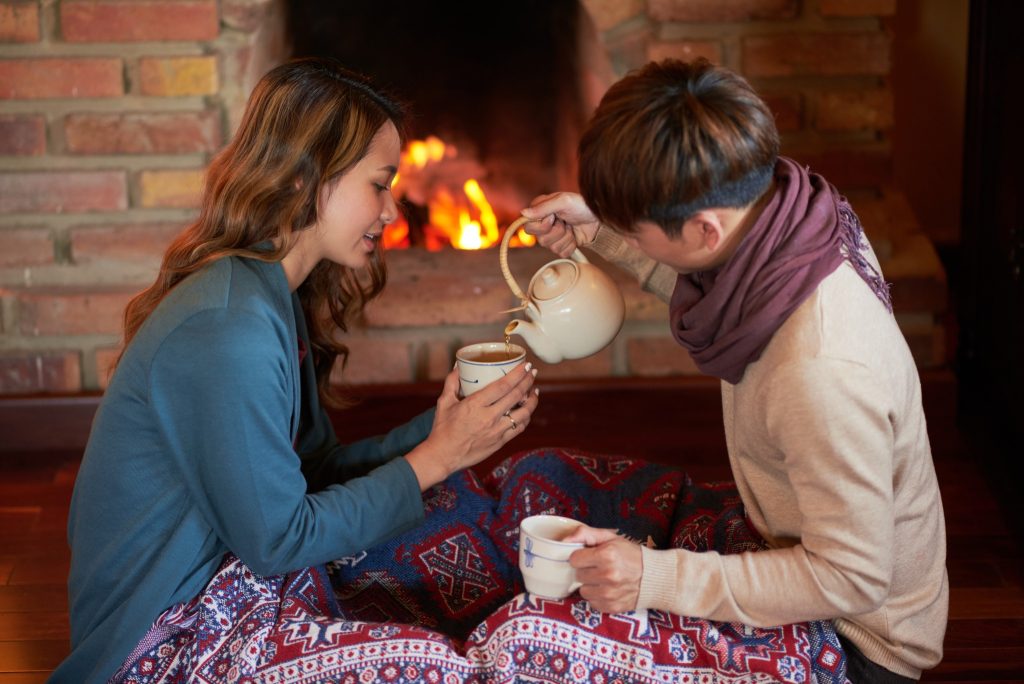 Image of two women sharing a pot of tea in front of a cozy fireplace.